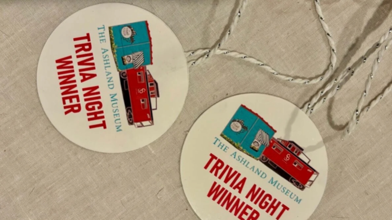 Round badge reading 'Trivia Night Winner' with a red train illustration and 'The Ashland Museum' text.