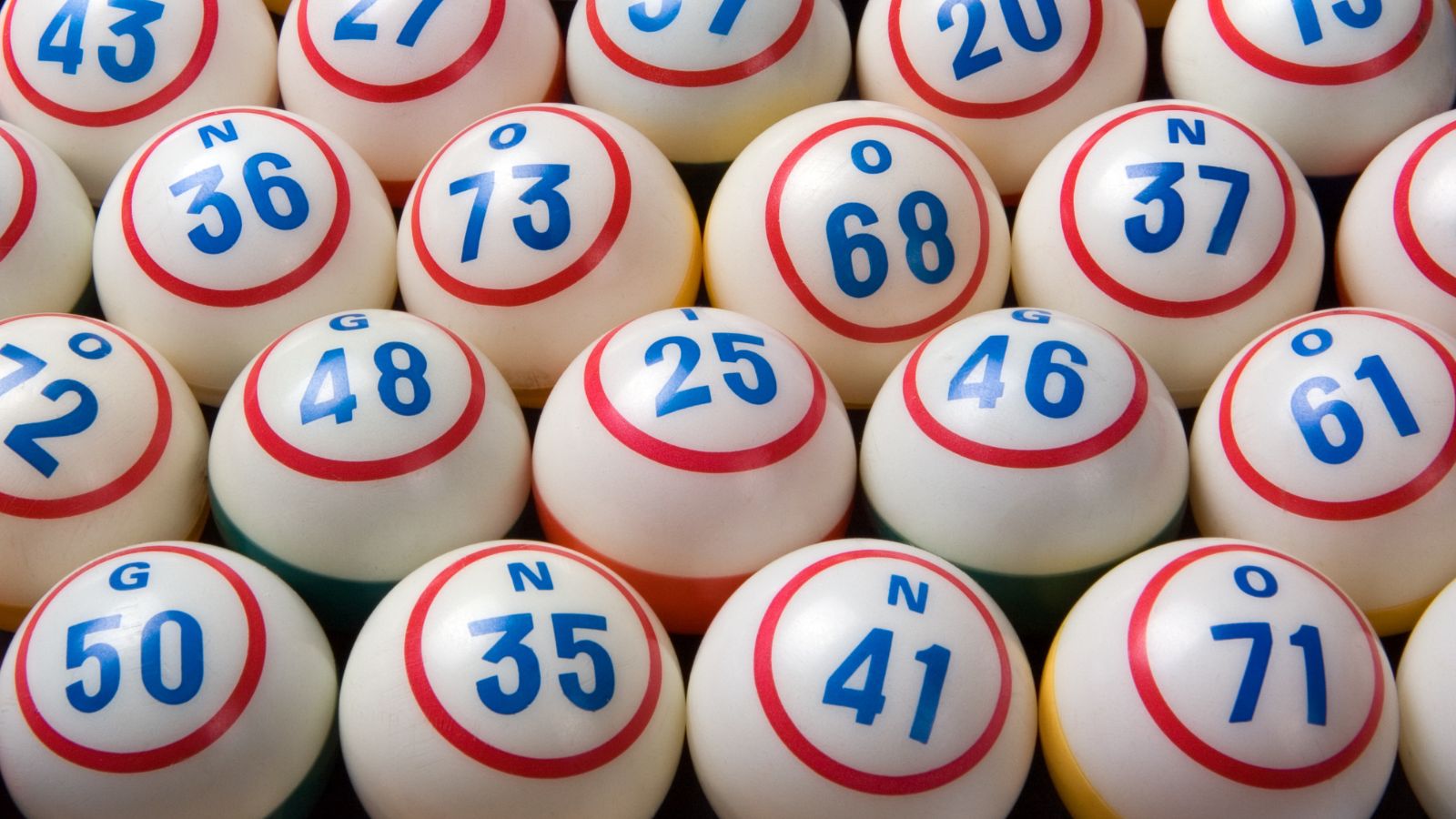 Cluster of white bingo balls with red rings and blue numbers visible in a close-up. It shows multiple balls with various numbers.